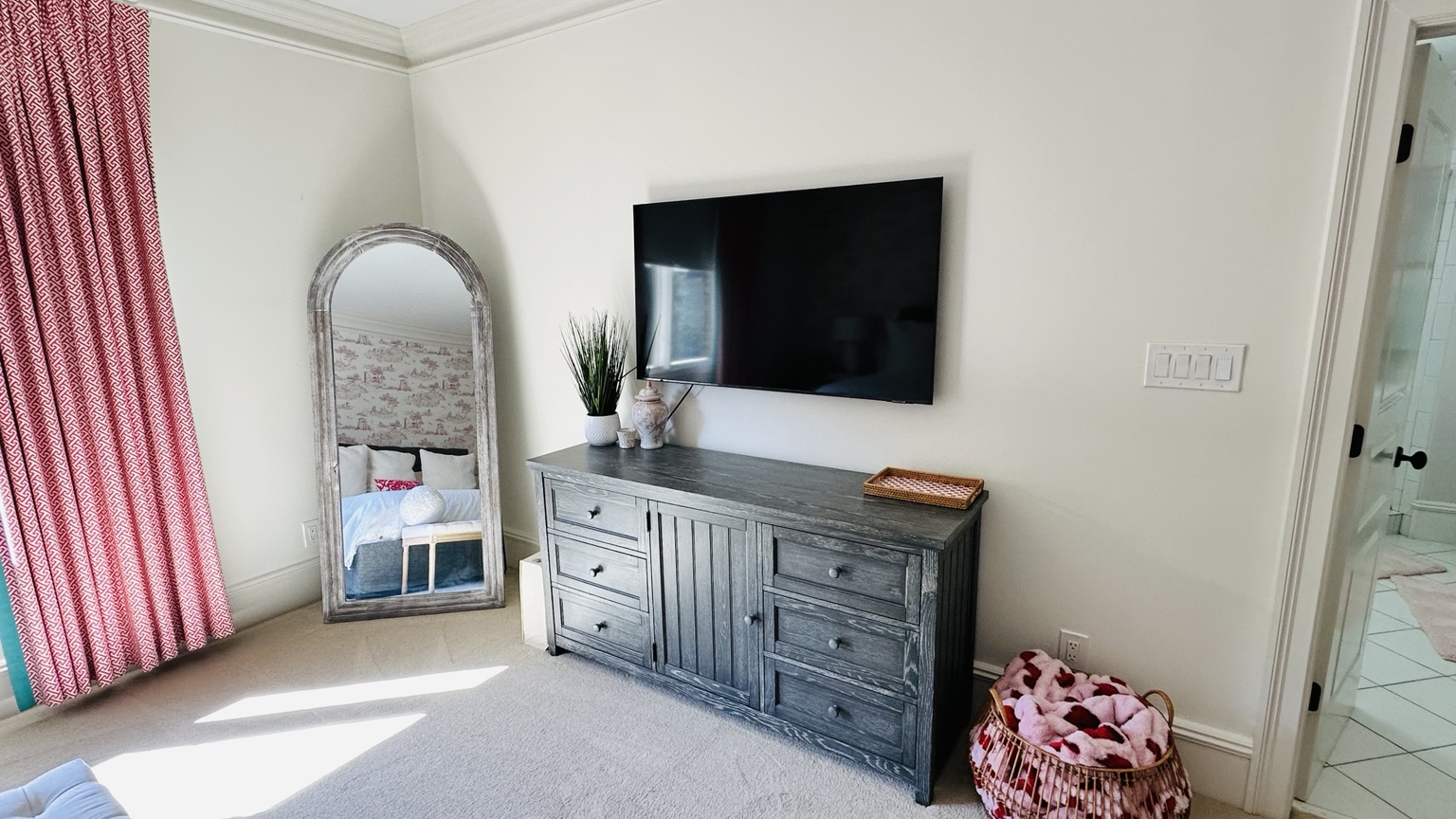 Wide bedroom view with dresser, mirror, television and pink decor