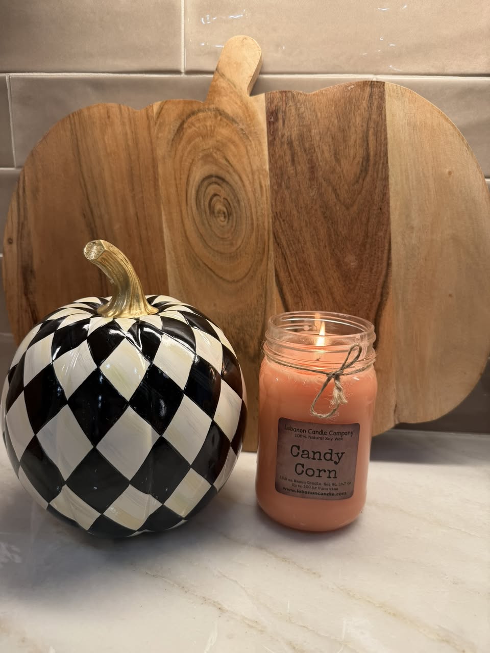 Lebanon Candle Company Candy Corn candle beside a black-and-white MacKenzie-Childs pumpkin and wooden pumpkin charcuterie board